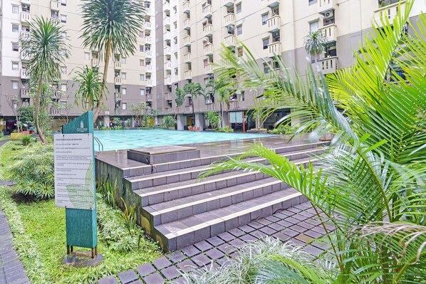A residential building with a swimming pool, steps leading to the pool, and surrounding greenery. - Capital O 93455 Apartement Gateway Cicadas By Az Pro Ii (Bandung)