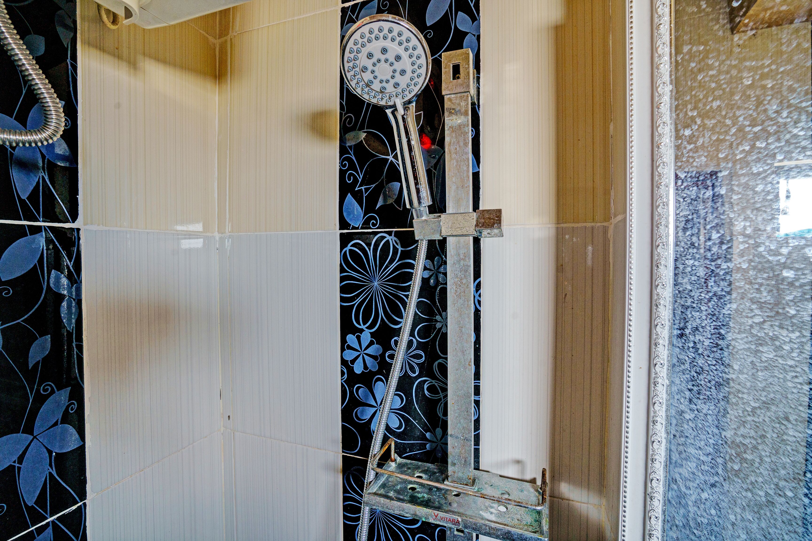 A shower with a handheld showerhead, a metal ladder, and a decorative shower curtain with a floral pattern.