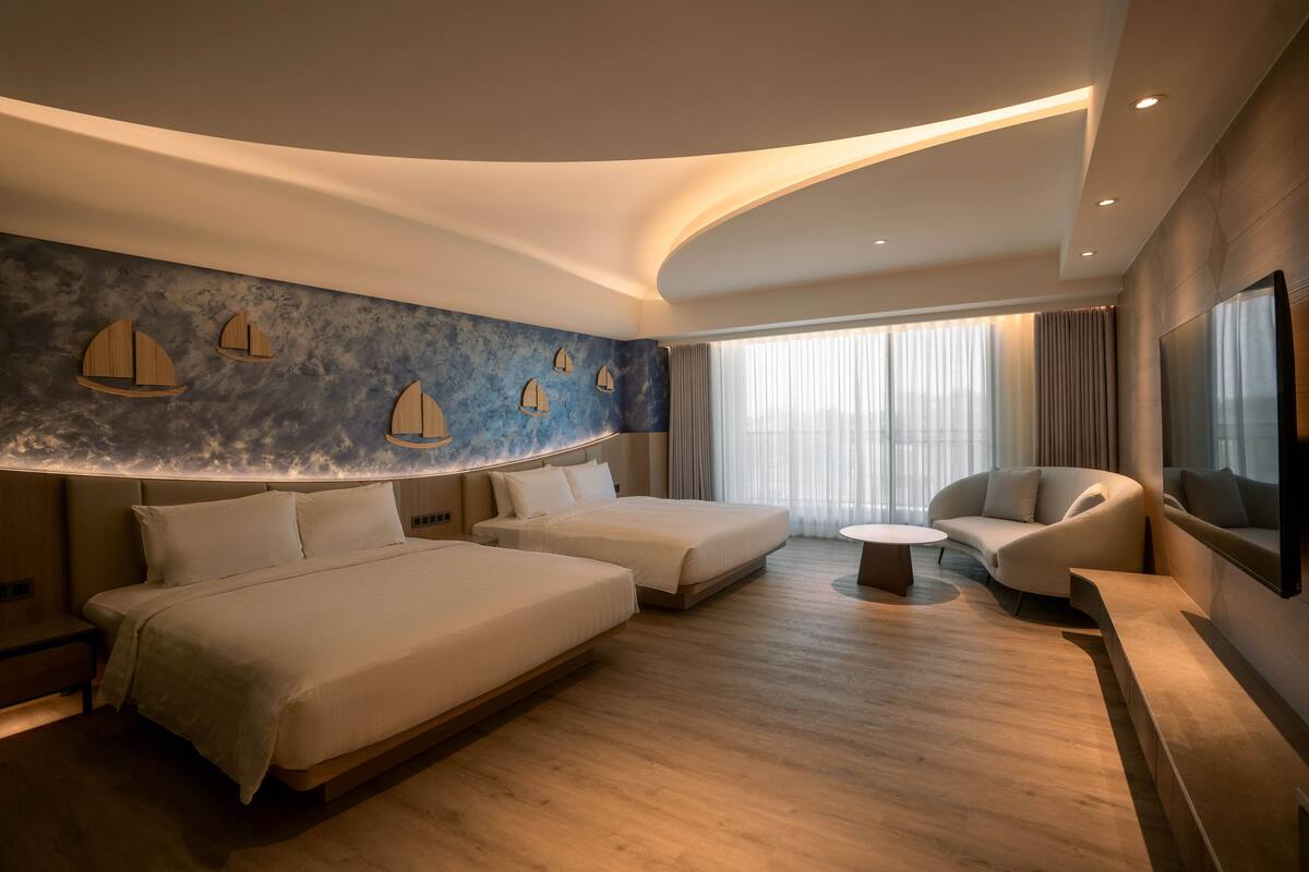 Una habitación de hotel moderna con dos camas, un sofá, una mesita y un televisor.