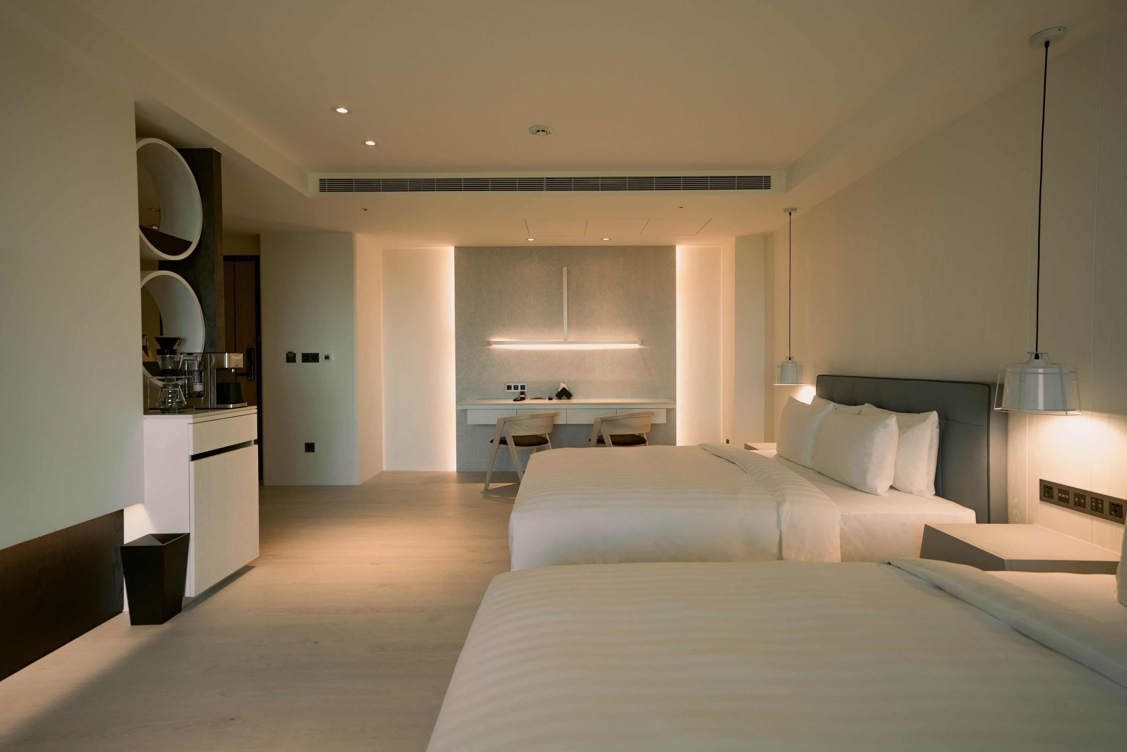 A modern hotel room with two beds, a desk, and a bathroom.