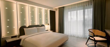 A modern hotel room with a large bed, a nightstand, a chair, and a large window with curtains.