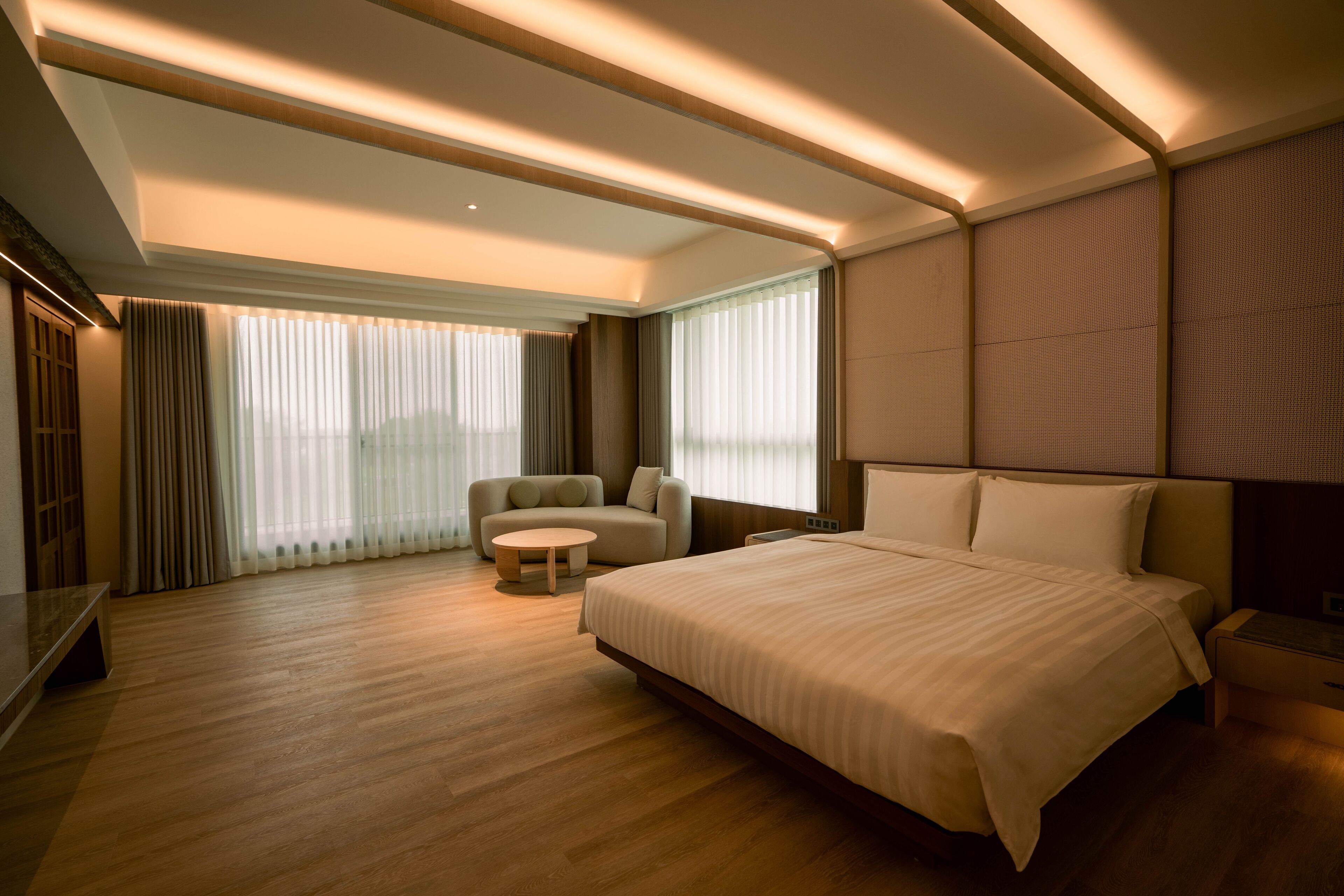 Habitación de hotel moderna con una cama grande, un sofá, una mesita redonda y un televisor.