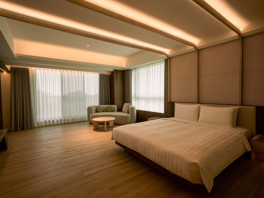 Habitación de hotel moderna con una cama grande, un sofá, una mesita redonda y un televisor.