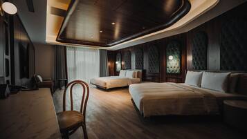 A modern hotel room with a wooden floor, a large bed, a smaller bed, a desk, and a chair.