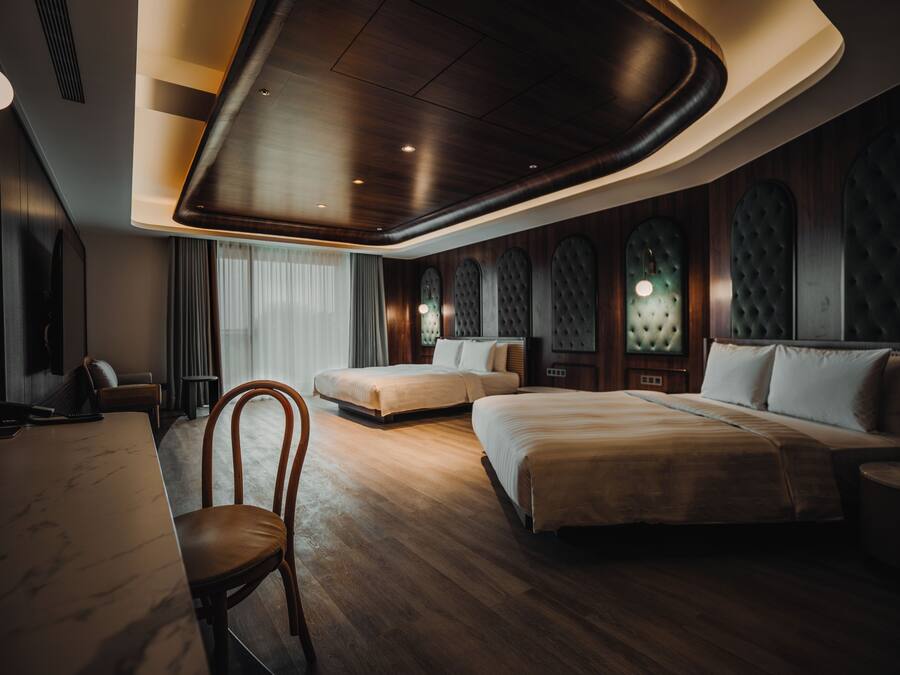 A modern hotel room with a wooden floor, a large bed, a smaller bed, a desk, and a chair.