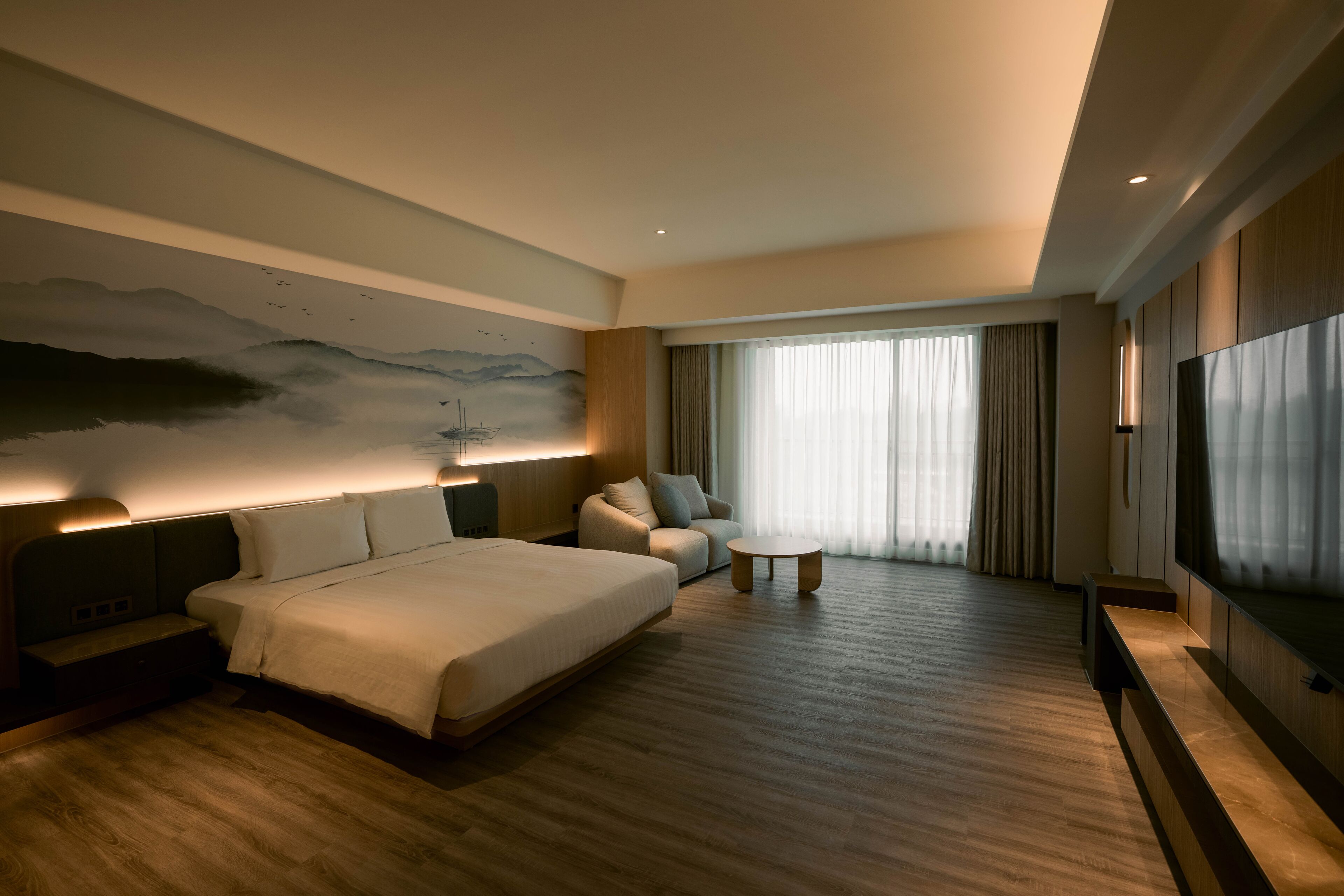 Ein modernes Hotelzimmer mit einem großen Bett, einer Couch, einem kleinen Tisch und einem Fernseher.