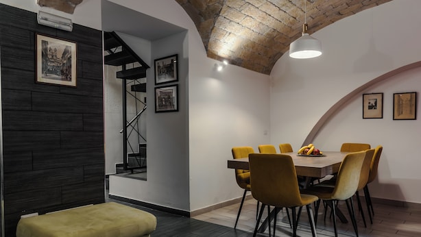 A dining area with a wooden table and yellow chairs, a staircase, and a cushioned bench. - Cozy guesthouse in the center of Rome (Roma)