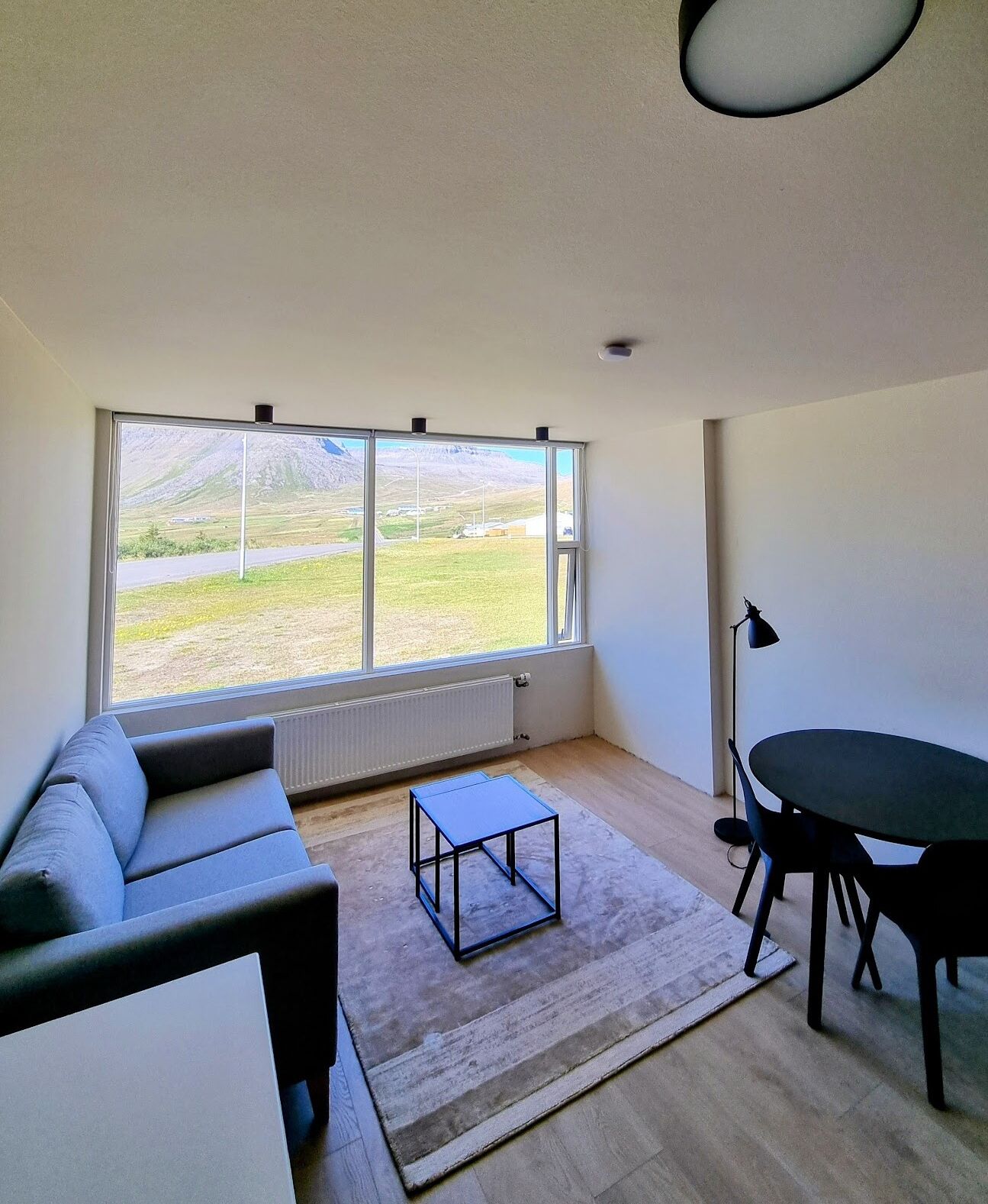 Una sala de estar moderna con un ventanal grande, un sofá, una mesa baja y una mesa de comedor con sillas.