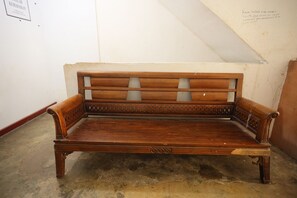 A wooden bench with intricate carvings, positioned in a room with a sloped ceiling and a concrete floor. - Hotel O Penginapan Alfafa ScorpioNearNagoya Hill Shopping Mall (Batam)