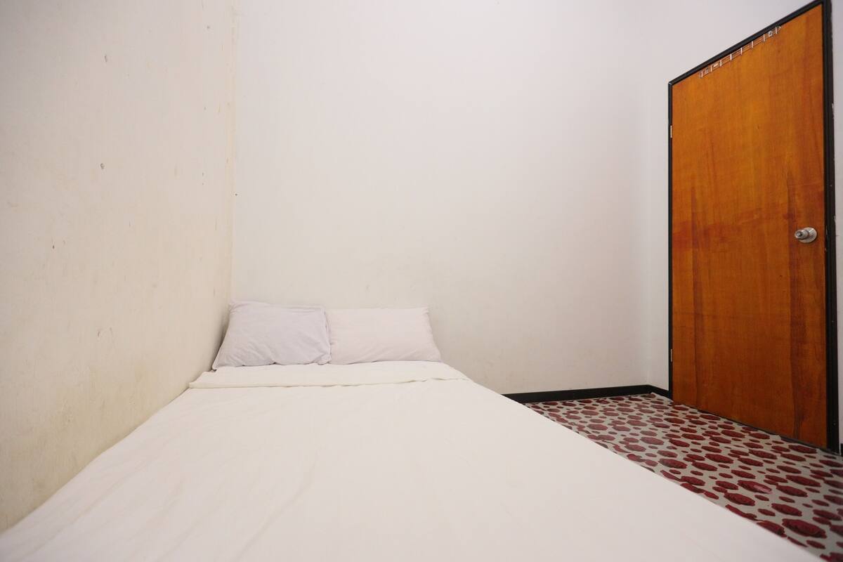 Een kleine kamer met een enkel bed, een houten deur en een vloer met patroon.