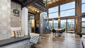 Una habitación amplia con suelo de madera, un comedor con mesa y sillas, y ventanas grandes que ofrecen vistas al exterior.