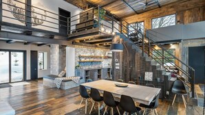Amplia sala de estar con una gran mesa de madera, sillas negras y una escalera que sube a un nivel superior.