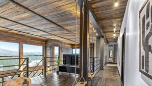 Amplia sala de estar con un gran ventanal que da a un paisaje pintoresco, un sillón colgante y un televisor de pantalla plana.