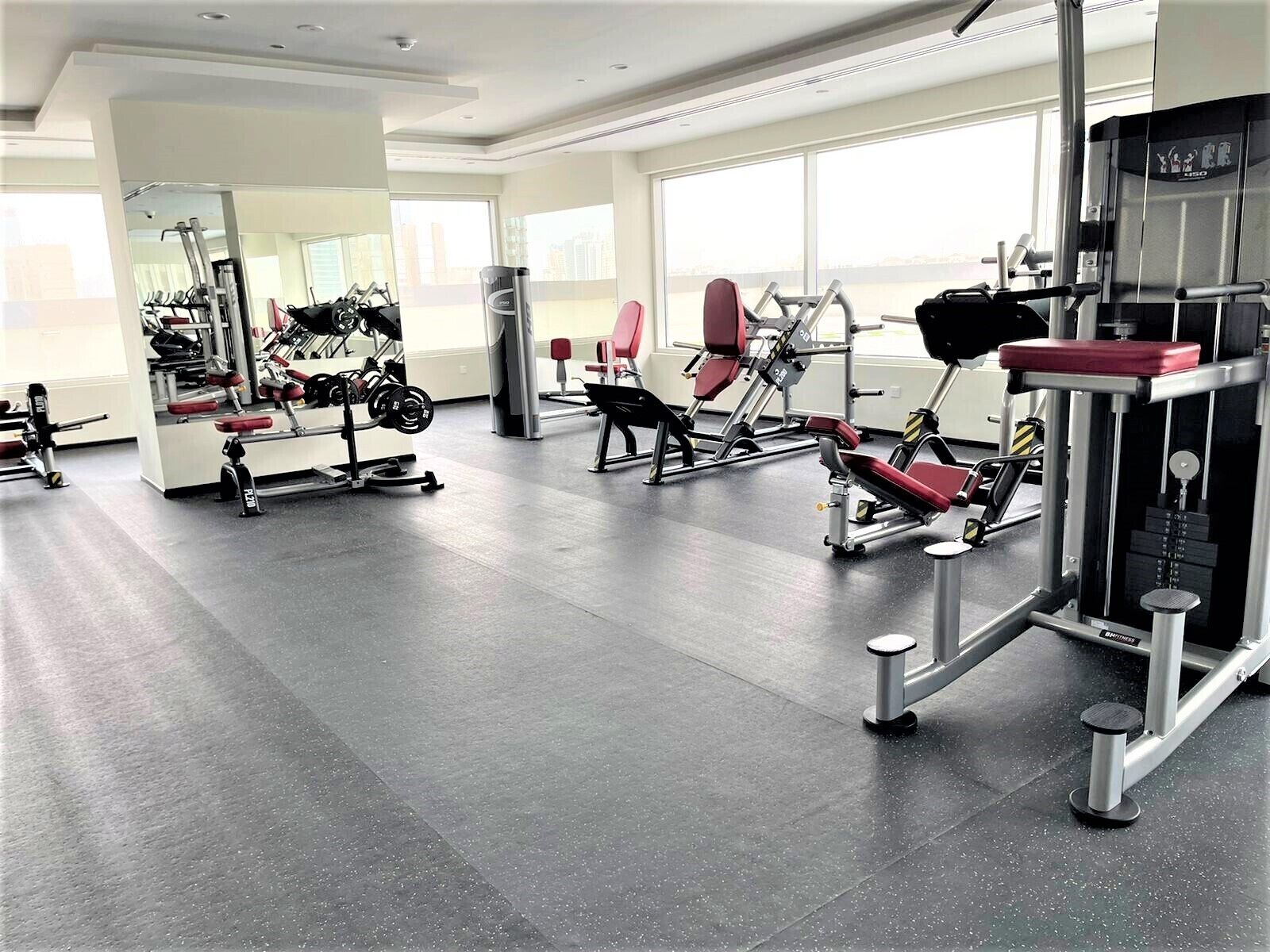 A gym with various exercise equipment, large windows, and a spacious layout.
