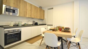Eine moderne Küche mit Holzschränken, einer eingebauten Mikrowelle, einem Backofen und einem Essbereich mit Holztisch und weißen Stühlen.