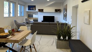 Ein modernes Wohnzimmer mit Sofa, Fernseher und Essbereich mit Stühlen und Tisch.