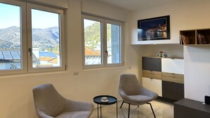 Ein modernes Wohnzimmer mit zwei Sesseln, einem kleinen Tisch, einem Flachbildfernseher und einem Bücherregal.