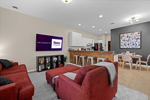 Una sala de estar moderna con un sofá rojo, una zona de cocina con armarios blancos y una mesa de comedor con sillas.