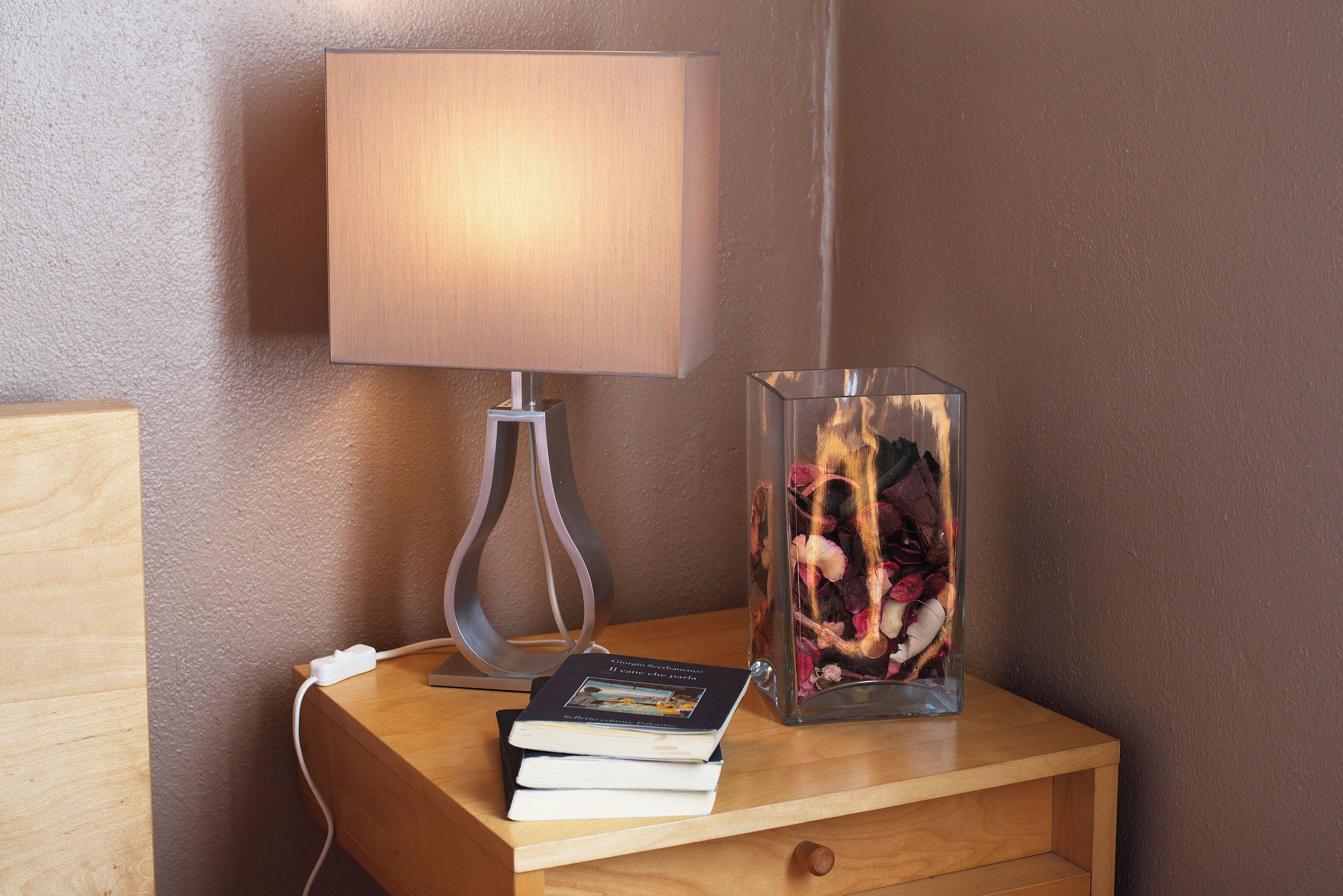 A bedside table with a lamp, a book, and a glass vase with flowers.