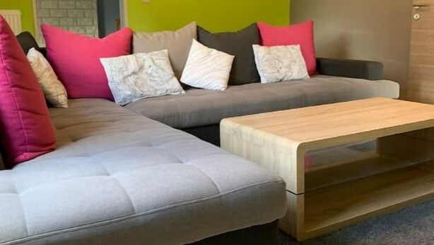 Un soggiorno moderno con un divano grigio, un tavolino in legno e una parete verde brillante.