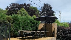 Zona patio esterna con pavimento in legno, un tavolo e sedie, e un pergolato con ombrellone.