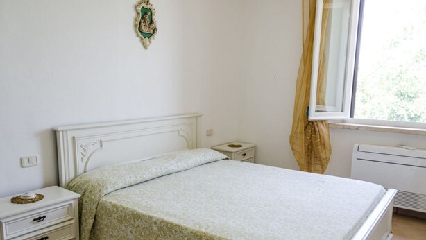 Une chambre avec un lit simple, une table de chevet, une commode, un radiateur et une fenêtre avec des rideaux.
