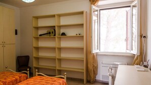Une chambre avec deux lits, une grande bibliothèque, une fenêtre avec des rideaux et un radiateur.