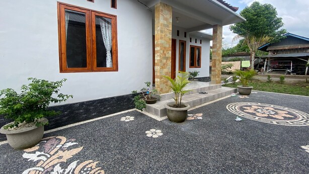 A house with a white exterior, wooden-framed windows, a stone pillar, and a paved entrance with floral patterns. - Hotel O Gians Homestay Near SMKN 2 Kuripan (Janapria)