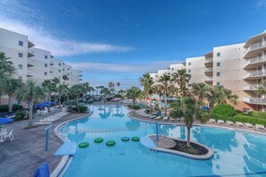 A swimming pool surrounded by palm trees and lounge chairs, with multi-story buildings in the background. - Beachfront Waterscape Condo, 2 King Suites, Bunk Room and Pools (Fort Walton Beach)