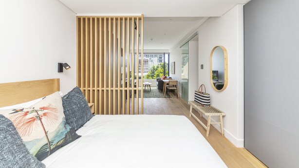 A modern bedroom with a bed, a wooden partition, a desk, and a chair. - Comfortable studio with city views (Cape Town)
