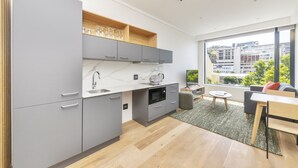 A modern kitchen with grey cabinets, a white countertop, and a built-in microwave. There is a window with a view of buildings and greenery. - Comfortable studio with city views (Cape Town)