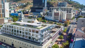 A modern building with a flat roof and multiple floors, surrounded by other buildings and a hilly landscape in the background. - Comfortable studio with city views (Cape Town)