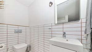 Un baño con inodoro, lavamanos, espejo y paredes con azulejos.