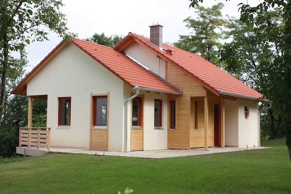 A single-story house with a red-tiled roof, wooden exterior, and a small porch.