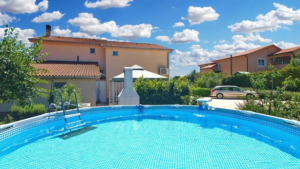 Une piscine dotée d’une terrasse carrelée, entourée de maisons et de verdure.