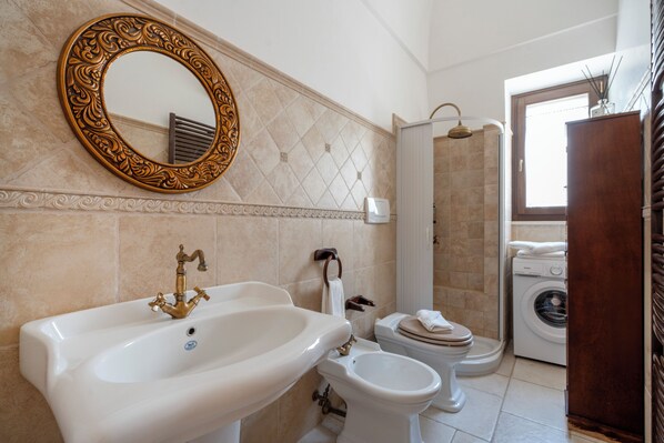 Une salle de bain avec un grand lavabo, deux toilettes, une douche et un lave-linge.