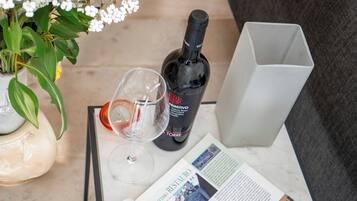 Un tavolo con una bottiglia di vino, un bicchiere di vino, un vaso con fiori e una rivista.