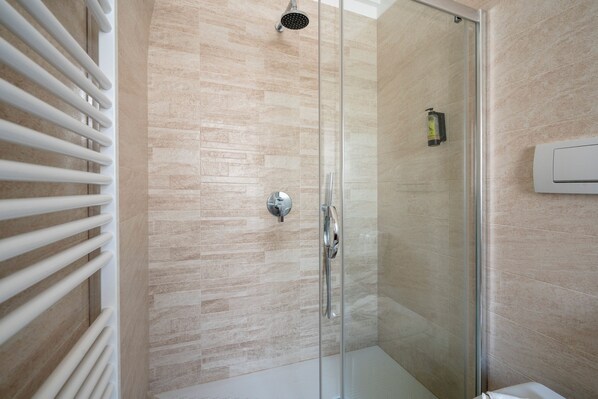A modern bathroom with a glass shower enclosure, a white radiator, and a wall-mounted air conditioning unit. - TRULLI CONTENTO ROOMS E APARTMENTS  (Alberobello)