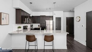 Une cuisine moderne avec des meubles en bois foncé, des appareils électroménagers en acier inoxydable et un grand îlot central doté de deux tabourets de bar.