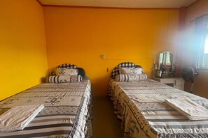 A room with two beds, each with striped bedding and checkered pillows, against a yellow wall.