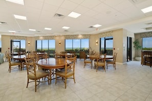 A spacious dining area with multiple round tables and chairs, large windows offering a view of the outdoors, and a ceiling with recessed lighting. - Beachfront 3BR condo with pool, wifi, and Marco Island views. (Marco Island)