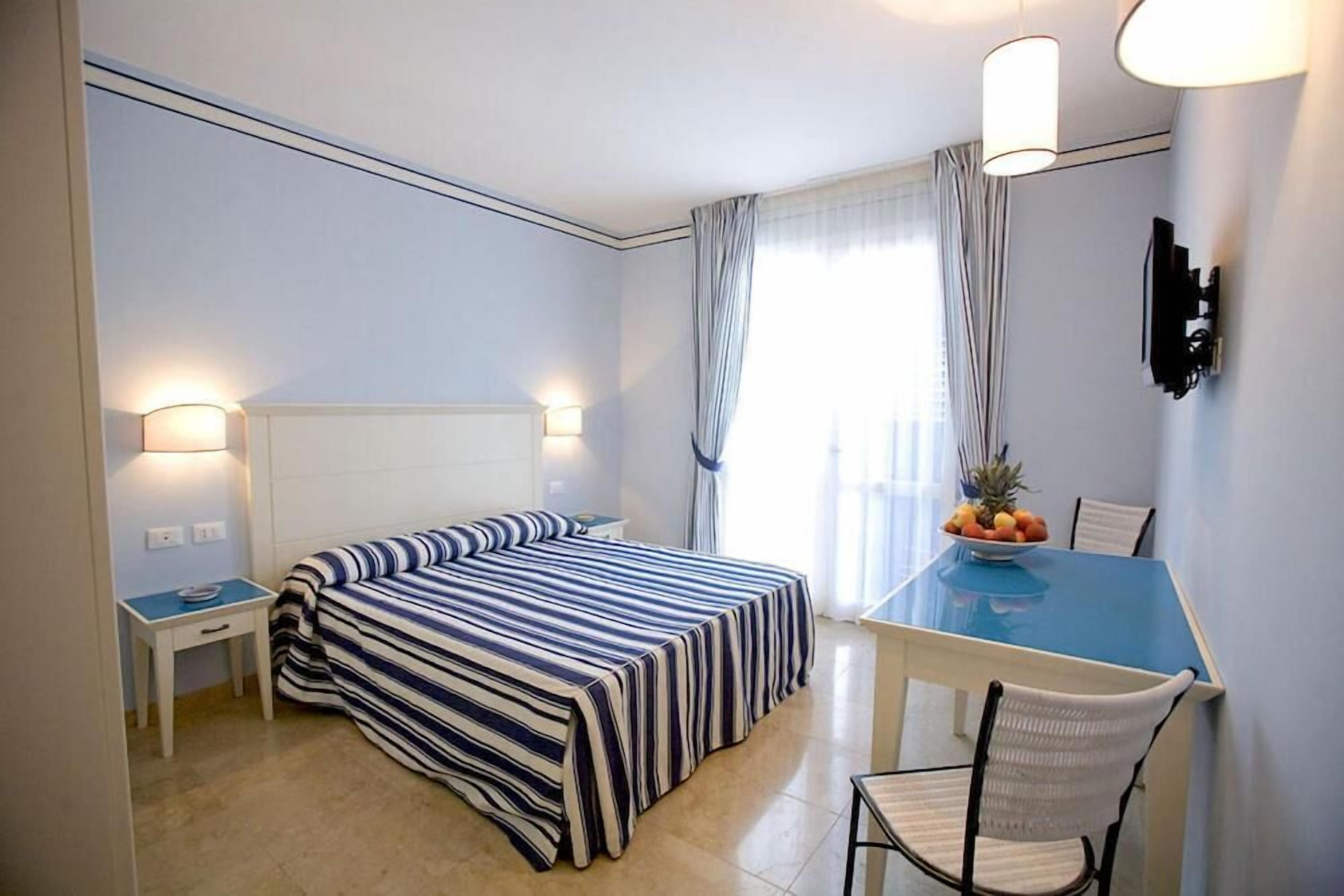 Habitación de hotel con cama, escritorio, silla, mesa con fruta y televisor en la pared.