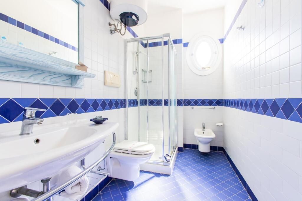 Une salle de bain avec un lavabo, des toilettes et un bidet blancs, une douche en verre et des murs recouverts de carreaux bleus.