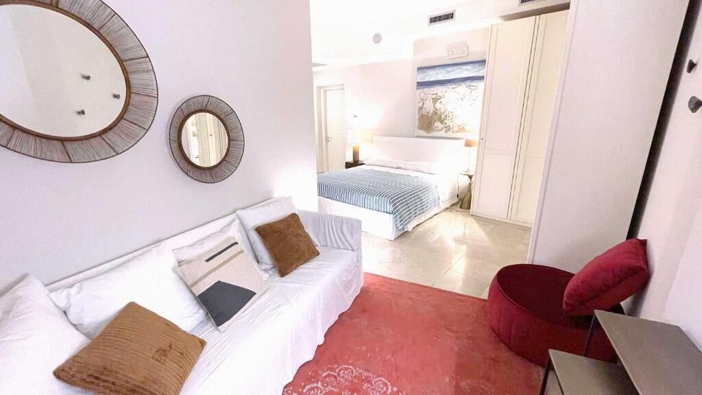 A bedroom with a bed, a white sofa, a red chair, and a mirror on the wall.