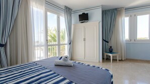 A hotel room with a bed, a TV mounted above it, and a small table with a vase. - Essence Favignana - Cala la Luna Resort (Favignana)