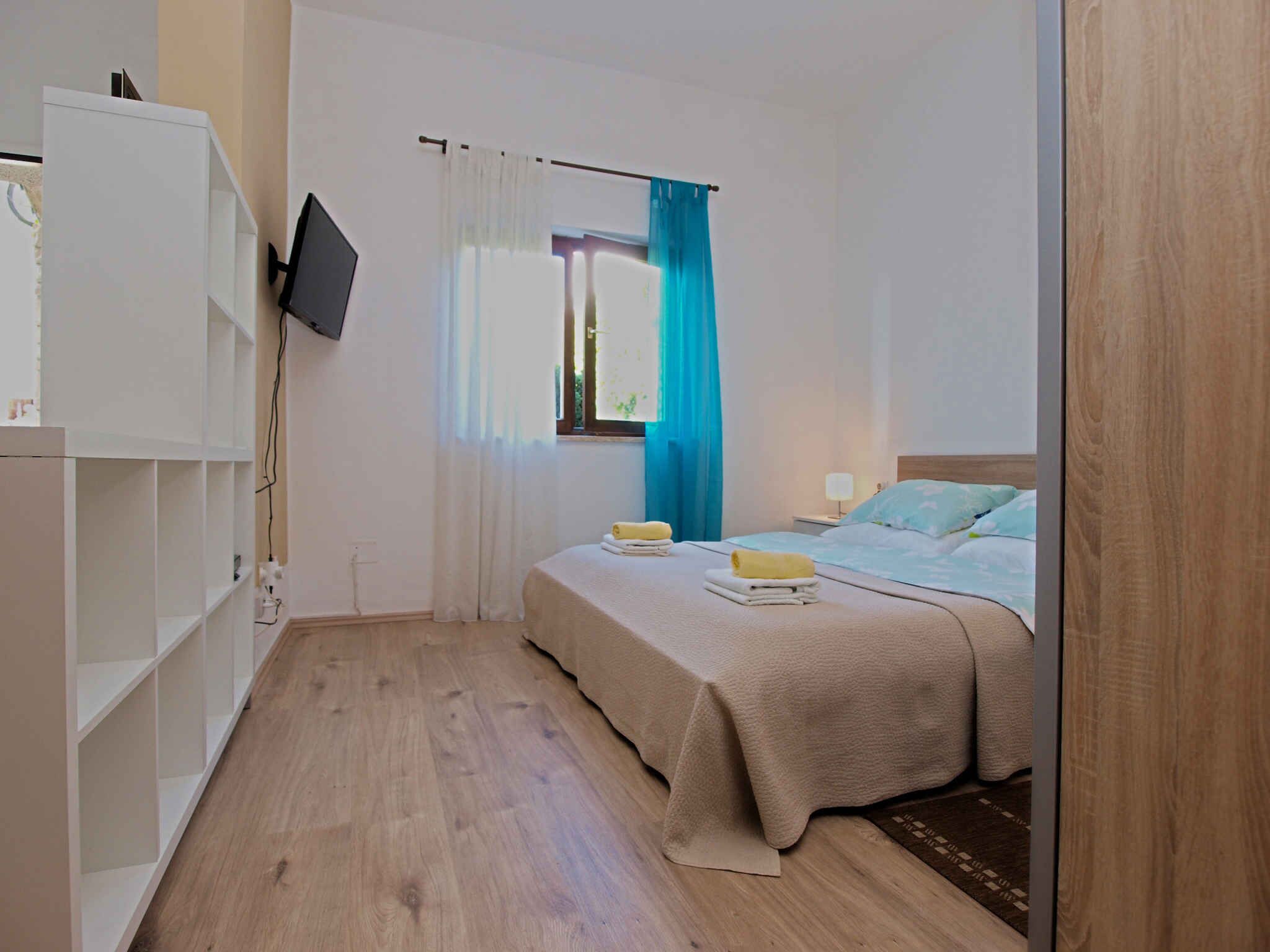 Ein Schlafzimmer mit einem Bett, einem an der Wand montierten Fernseher, einem Kleiderschrank und einem Fenster mit Vorhängen.