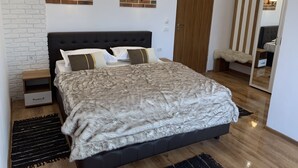 A bedroom with a large bed, a wooden wardrobe, a mirror, and two wall-mounted light fixtures. - CONACUL FLO'CAMY (Dragus)