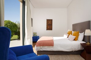 Een hotelkamer met een bed, een blauwe fauteuil, een nachtkastje en een raam met uitzicht op groen.