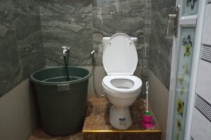 Et badeværelse med toilet, en grøn skraldespand og en lyserød toiletbørste.