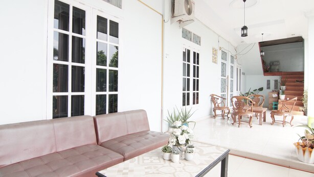 A spacious living area with a red sofa, a coffee table, and several wooden chairs. There are large windows and a TV mounted on the wall.